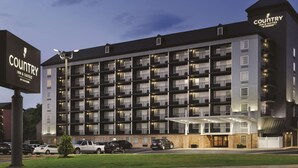 A multi-story hotel with a modern design, featuring balconies on each floor, a covered entrance, and a parking area with several cars. - Country Inn & Suites by Radisson, Pigeon Forge South, TN (Pigeon Forge)