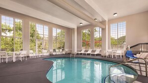 An indoor swimming pool with clear views of trees through large windows, surrounded by white lounge chairs and tables. - Country Inn & Suites by Radisson, Pigeon Forge South, TN (Pigeon Forge)