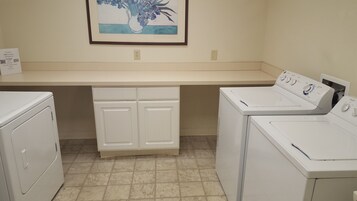 A laundry room with two washing machines, a dryer, and a countertop with a framed picture.
