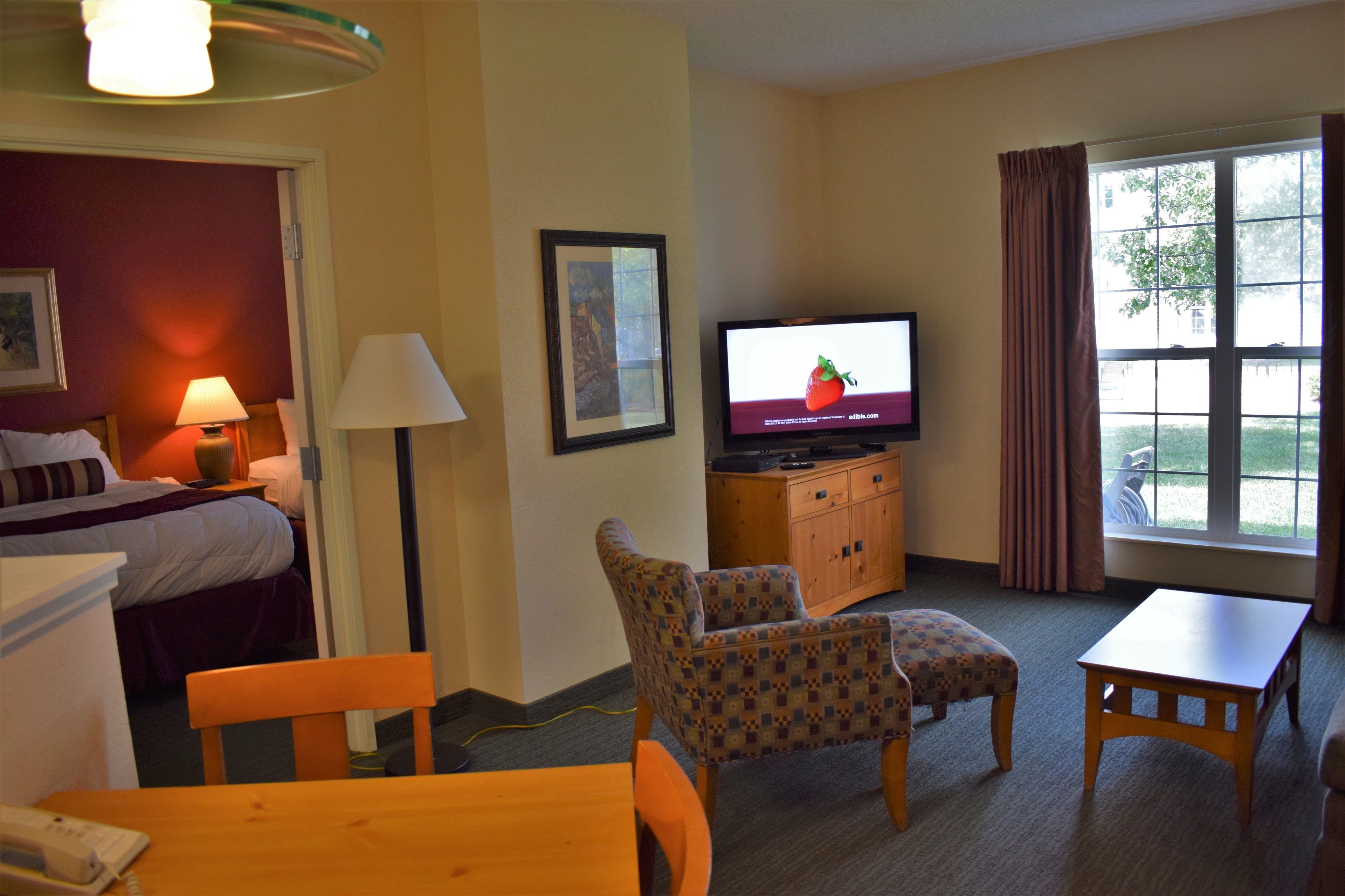 A hotel room with a bed, a TV, a desk, a chair, and a window with curtains.