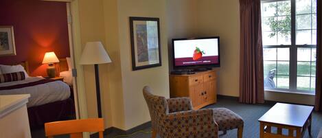 A hotel room with a bed, a TV, a desk, a chair, and a window with curtains.