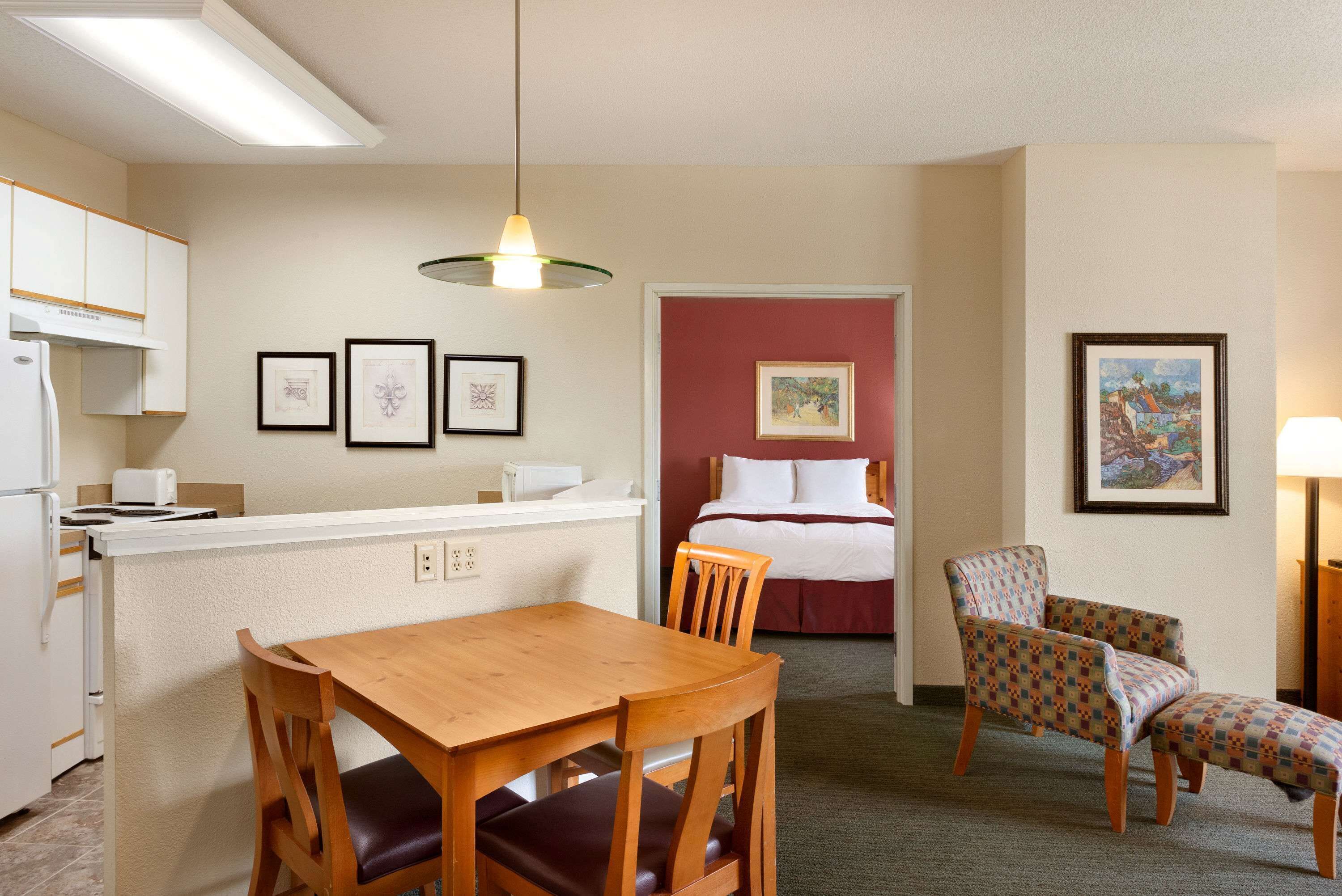 A compact hotel room with a kitchenette, a dining area, a bed, and a seating area.