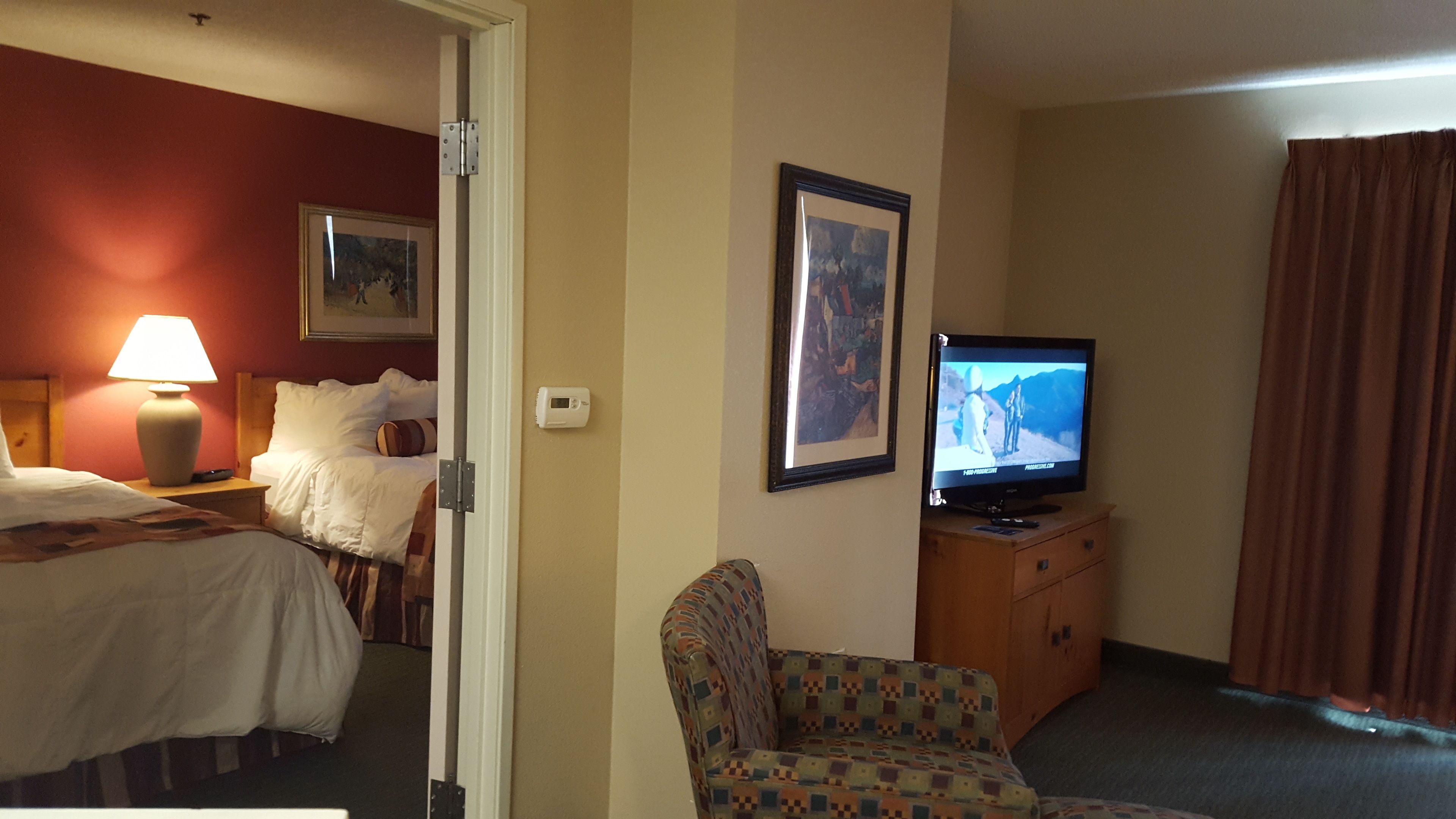 A hotel room with a bed, a chair, a television, and a painting on the wall.