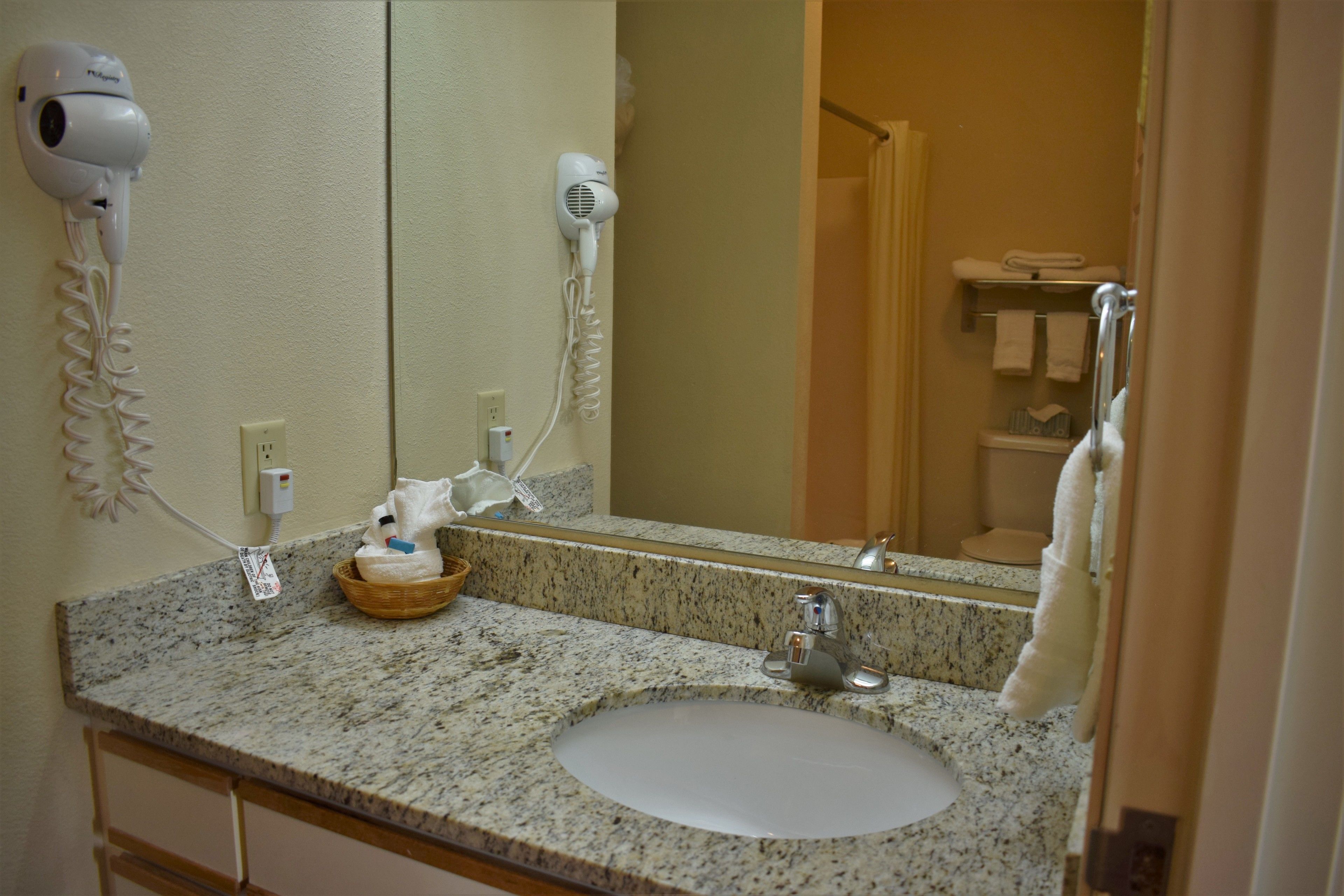 A bathroom with a granite countertop, a sink, a mirror, a hairdryer, and a towel rack.