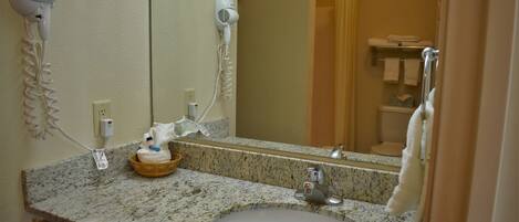 A bathroom with a granite countertop, a sink, a mirror, a hairdryer, and a towel rack.
