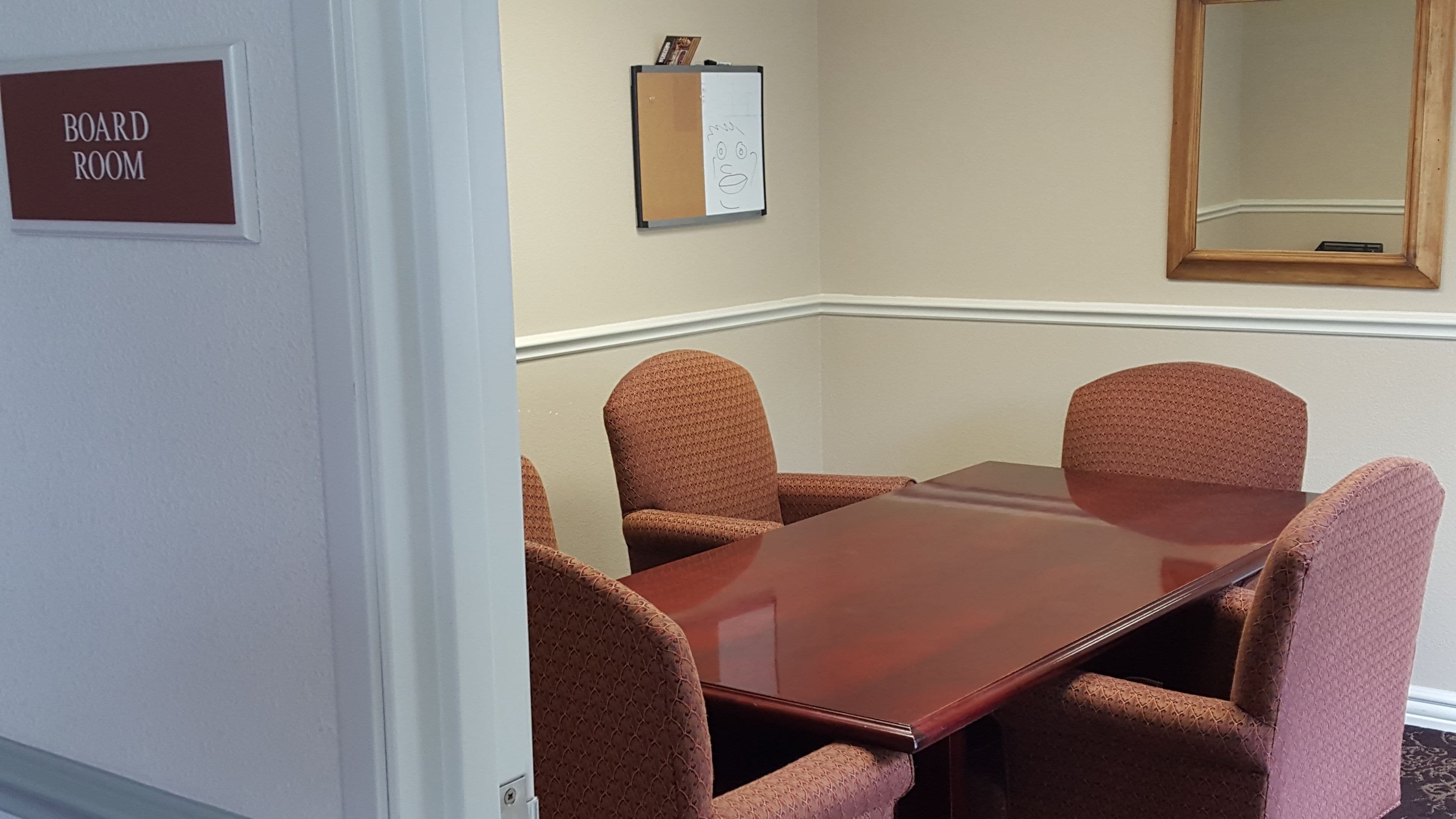 A board room with a wooden table and four patterned chairs. A sign on the wall reads "BOARD ROOM."