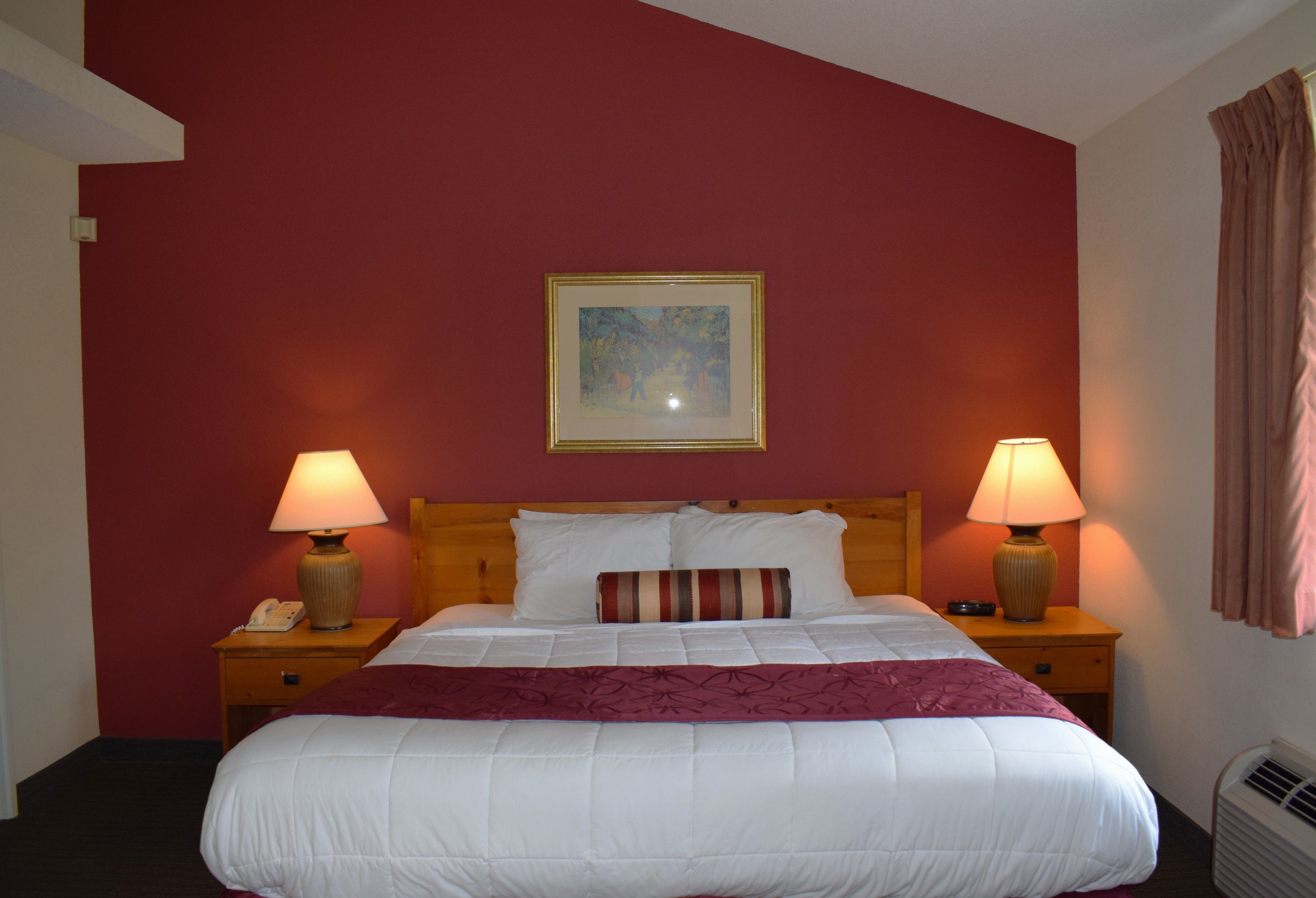 Habitació d'hotel amb un llit gran, dues làmpades de nit, un quadre a la paret i una paret decorativa vermella.