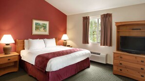 A hotel room with a large bed, two bedside lamps, a television on a wooden cabinet, a window with curtains, and a painting on the wall.