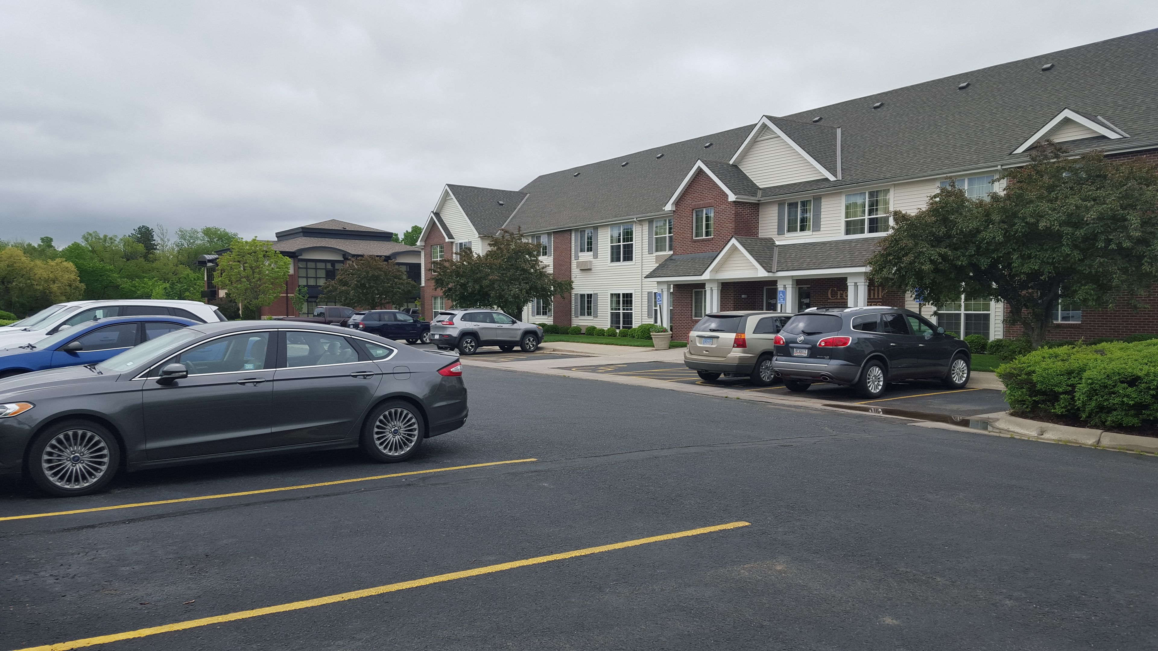 A parking lot with several cars parked in front of a building with a brick facade and a sloped roof.