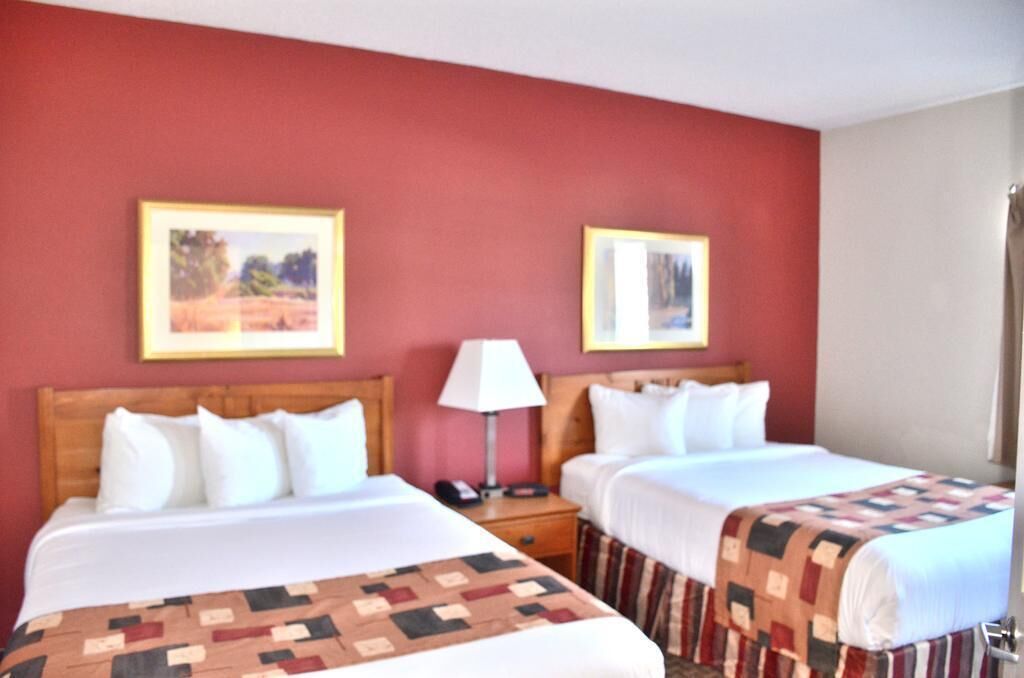A hotel room with two beds, a wooden headboard, a nightstand with a lamp, and two framed pictures on the wall.