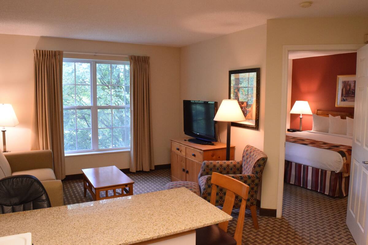 A hotel room with a bed, a television, a desk, a chair, a sofa, and a window with curtains.