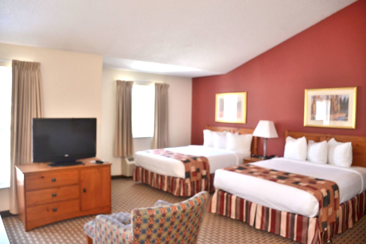 A hotel room with two beds, a TV, a desk, and a chair.