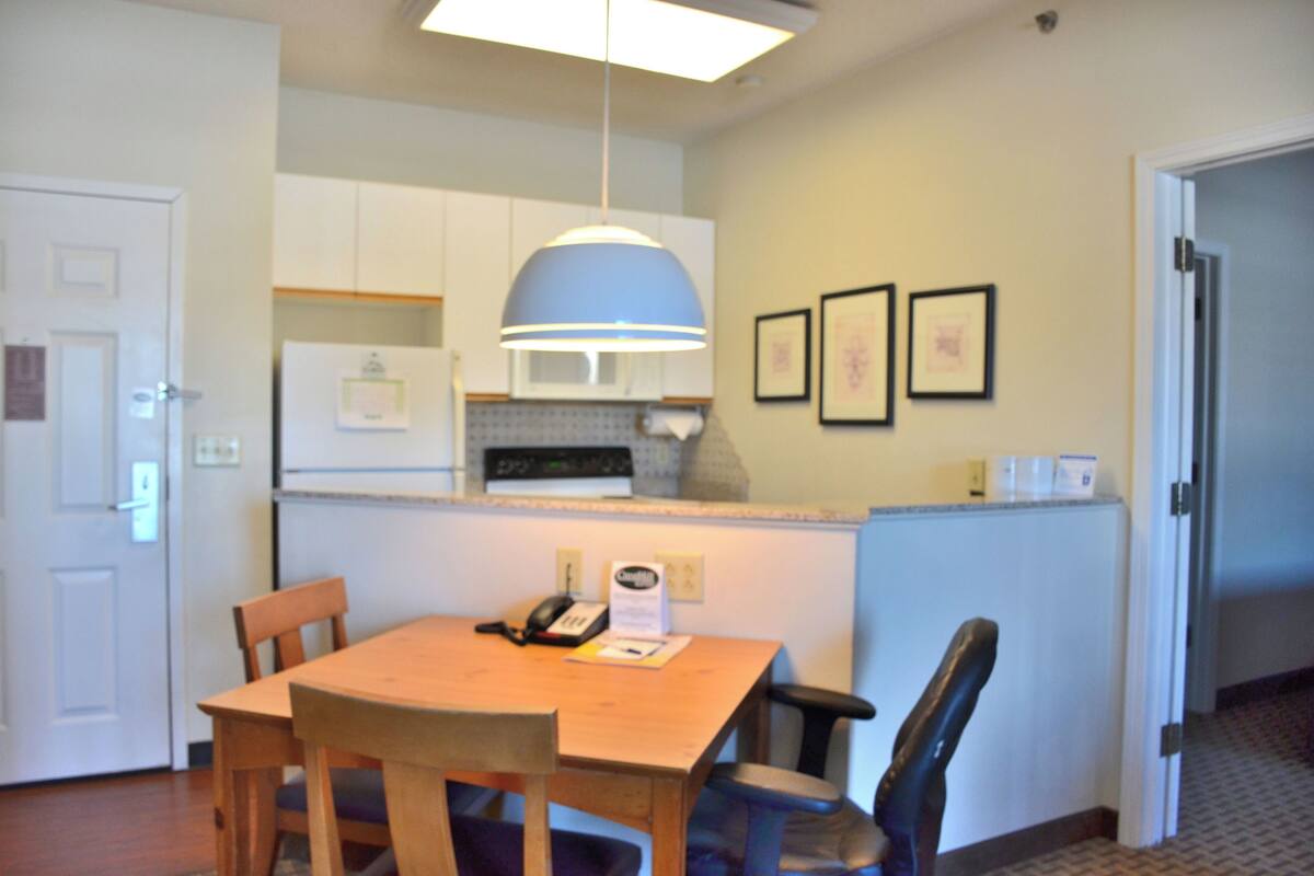 A compact kitchen with white cabinets, a wooden dining table, and a blue pendant light.