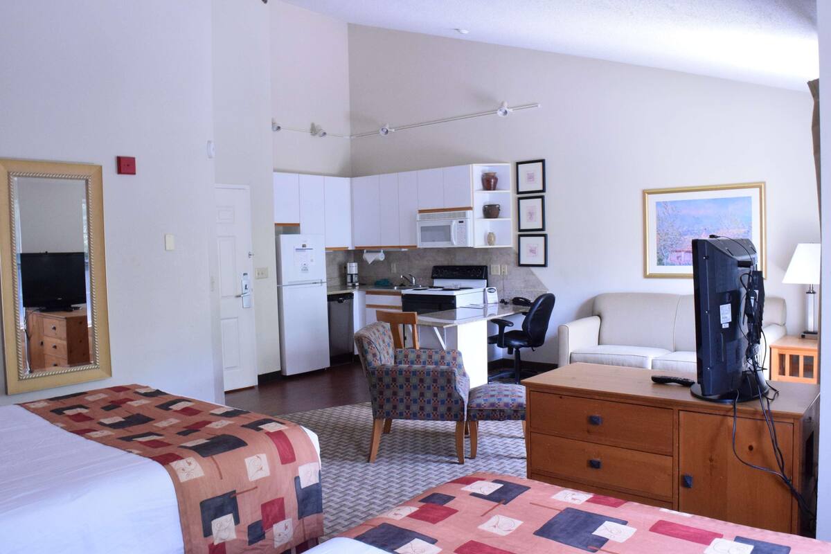A compact hotel room with a bed, a desk, a chair, a television, and a kitchenette.
