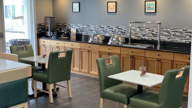 A modern restaurant with green upholstered chairs, a black countertop, and a tiled backsplash. - Cresthill Suites Syracuse (East Syracuse)
