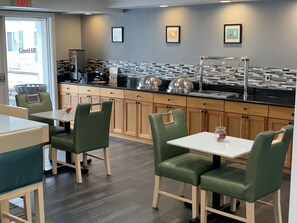 A modern restaurant with green upholstered chairs, a black countertop, and a tiled backsplash. - Cresthill Suites Syracuse (East Syracuse)