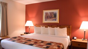 A hotel room with a large bed, two bedside tables, a nightstand, a painting on the wall, and a window with curtains. - Cresthill Suites Syracuse (East Syracuse)