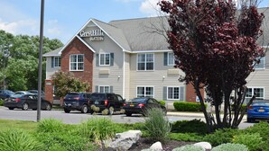 A Crest Hill Suites hotel with a brick facade, multiple windows, and a parking lot with several cars. - Cresthill Suites Syracuse (East Syracuse)