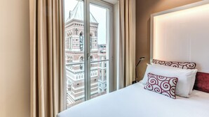 A hotel room with a large window, a bed with patterned pillows, and a view of a historic building. - La Griffe Hotel (Rome)