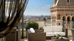 A rooftop terrace with wicker furniture and a view of a historic building with arches and a cross. - La Griffe Hotel (Rome)