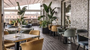An outdoor dining area with tables and chairs, large potted plants, and a view of buildings in the background. - La Griffe Hotel (Rome)