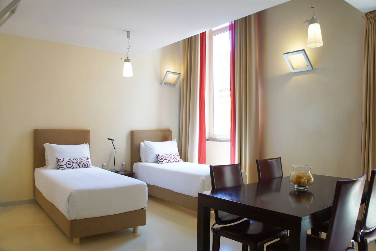 Hotellihuone, jossa on kaksi sänkyä, ruokapöytä ja pöydällä maljakko.