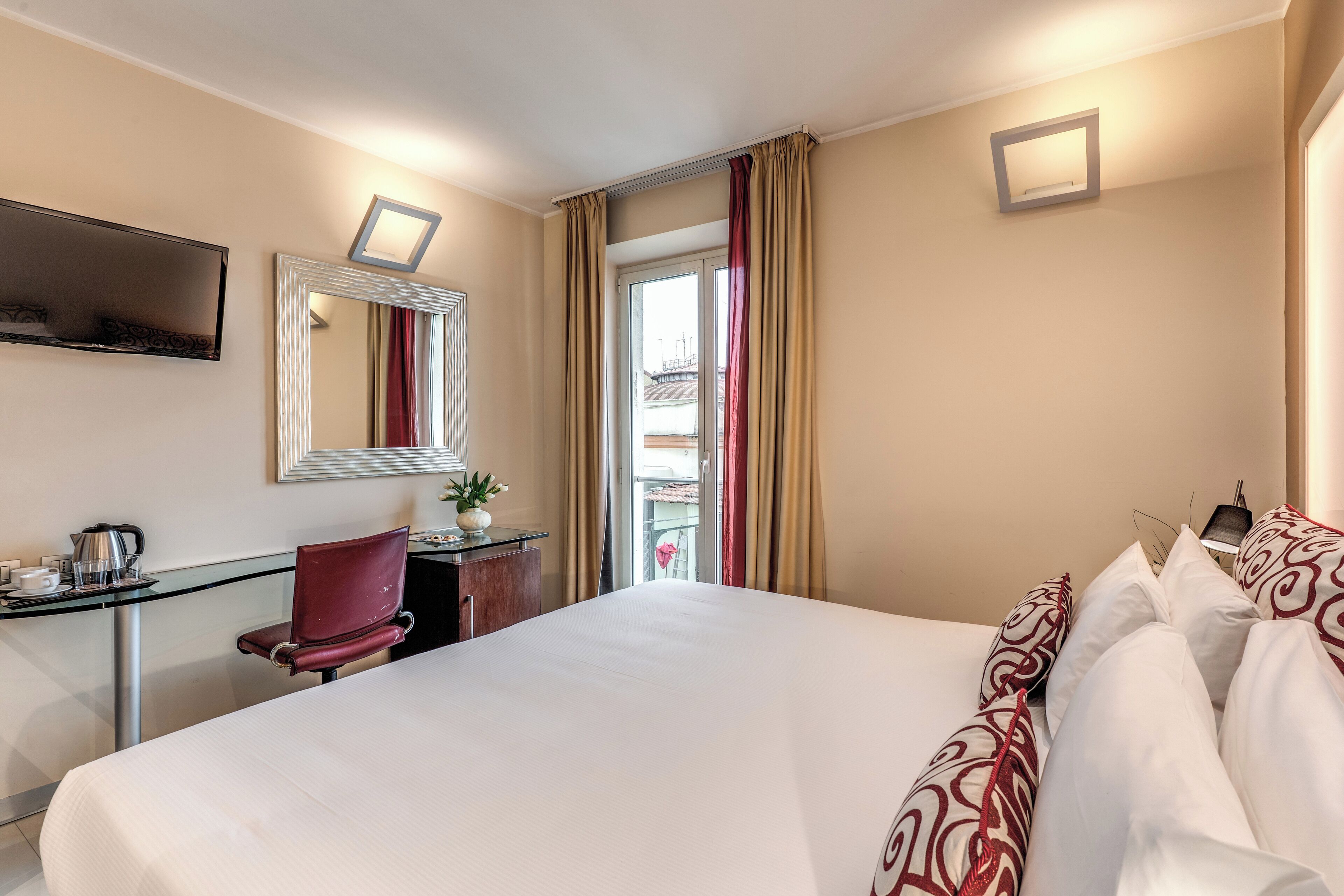 A hotel room with a large bed, a desk with a chair, a television, and a window with curtains.