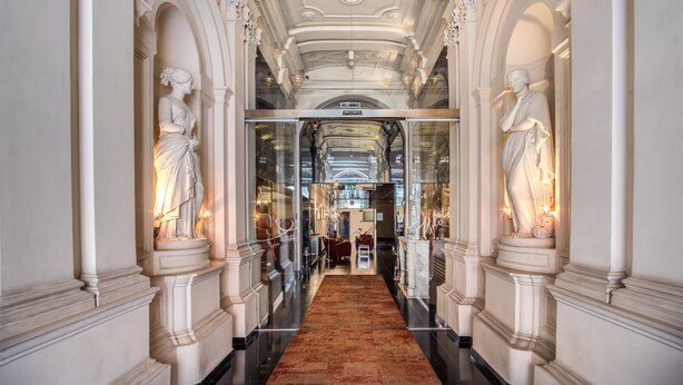 A grand hallway with classical architecture, including statues and ornate ceiling details. - La Griffe Hotel (Rome)