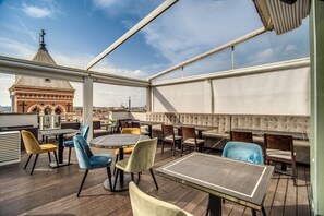 Una terrazza sul tetto con tavoli e sedie rotonde, vista su un edificio storico e cielo sereno.