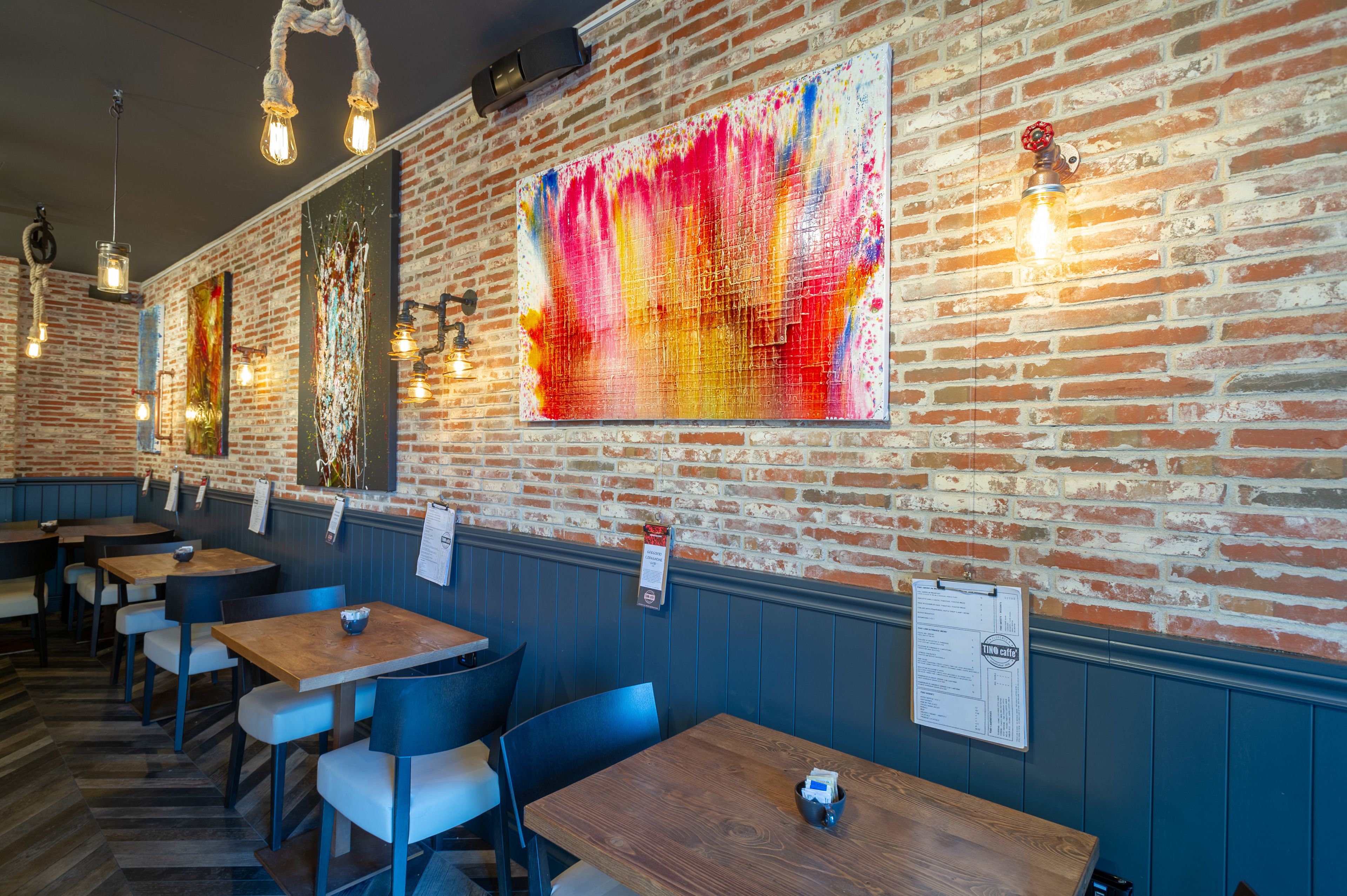 Interior de restaurante con paredes de ladrillo, mesas de madera y sillas azules.