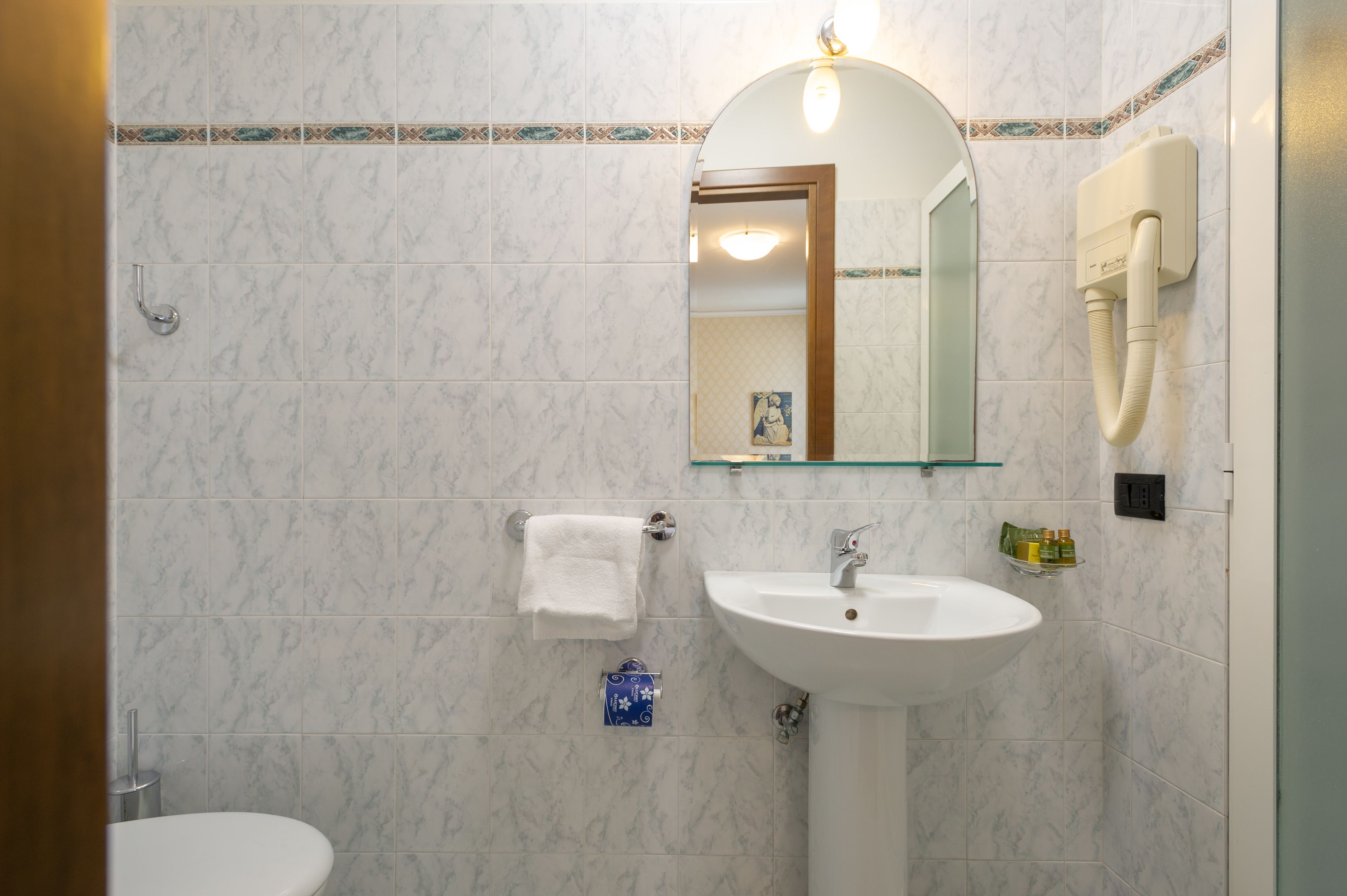 Un bagno con lavandino bianco, specchio, portasciù asciugamani e water.