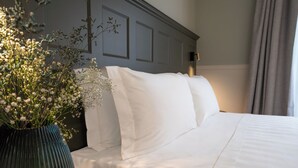 A neatly made bed with white linens, a dark green vase with white flowers, and a wall-mounted light fixture. - Il Malaspina (Florence)