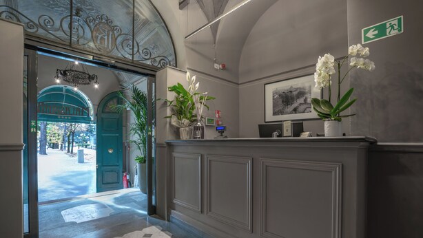 A reception area with a check-in counter, a green door, potted plants, and a framed picture on the wall. - Il Malaspina (Florence)