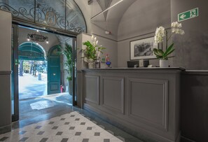 Zona de recepción con mostrador de check-in, una puerta verde, plantas en macetas y un cuadro en la pared.