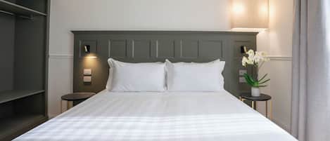 Una cama bien hecha con sábanas blancas, un cabecero oscuro y una lámpara de noche.