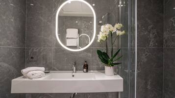 Un bagno moderno con un lavandino bianco, uno specchio con illuminazione circolare e un'orchidea in vaso.