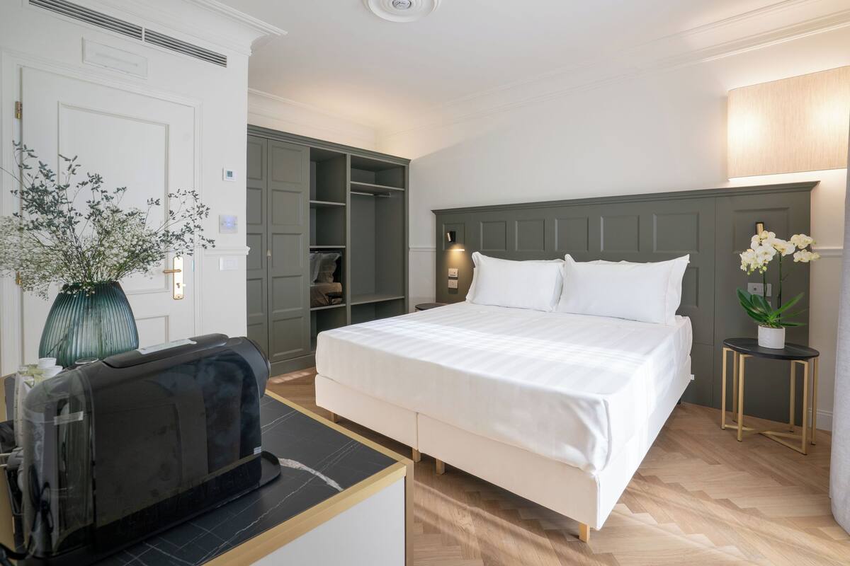 Ein Hotelzimmer mit einem großen Bett, einem eingebauten Kleiderschrank, einem Nachttisch mit Lampe und einer kleinen Topfpflanze.