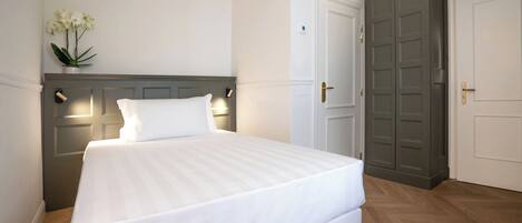 A neatly made bed with a white mattress and pillows, a bedside lamp, and a small plant on the nightstand.