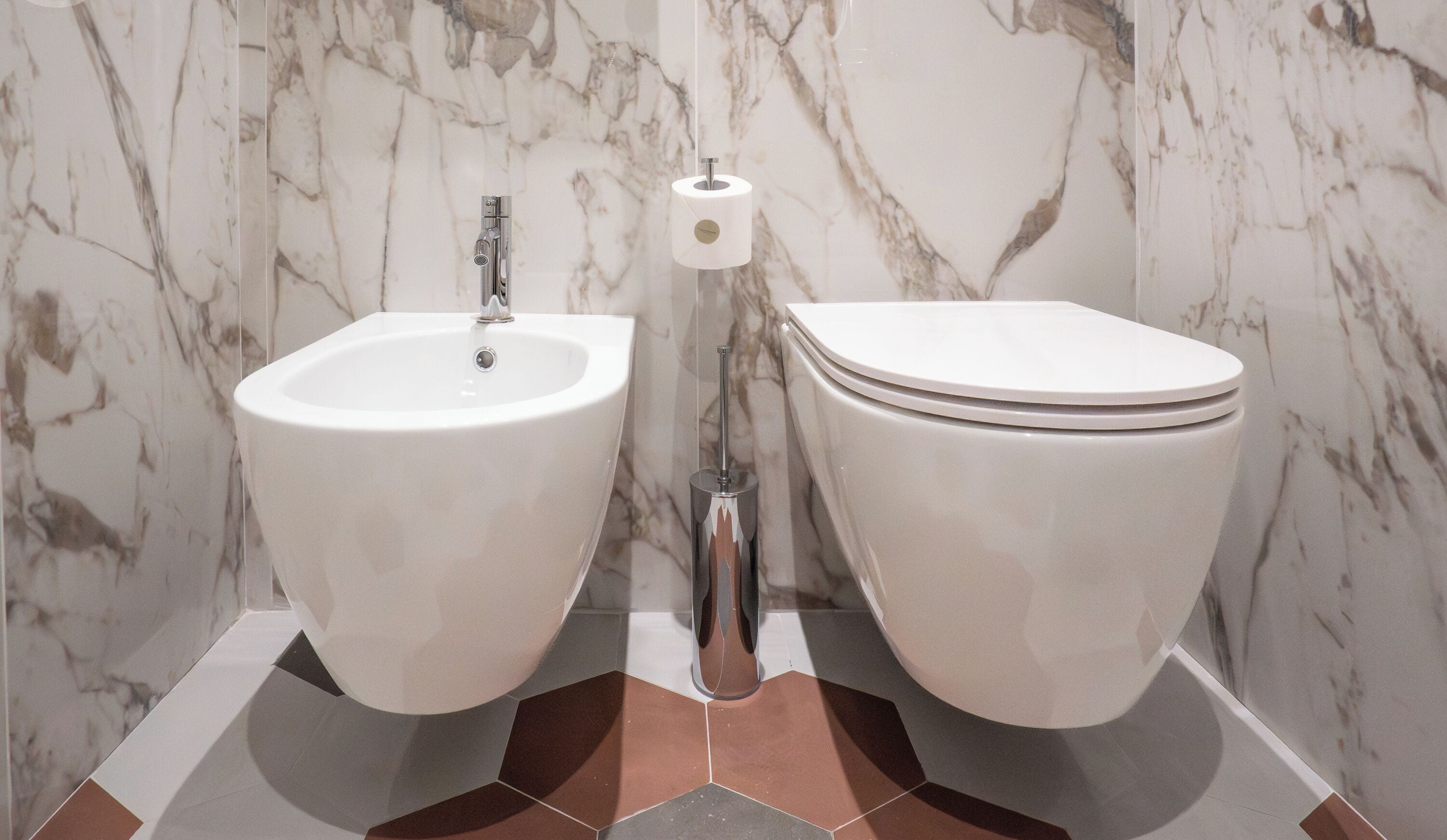 A bathroom with a bidet, toilet, and marble walls.