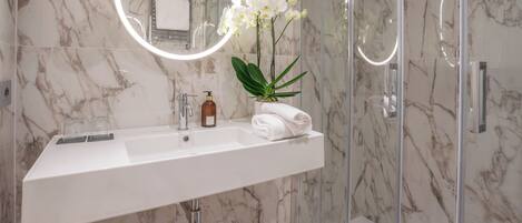 A bathroom with a marble sink, a mirror with a light, and a shower area.