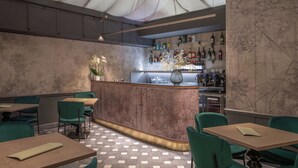 A restaurant with a bar area, green upholstered chairs, and a patterned floor. - Il Malaspina (Florence)