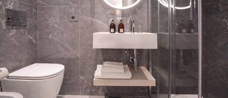Un baño moderno con un inodoro, un lavamanos con dos botellas, un vaso y una toalla sobre una repisa.