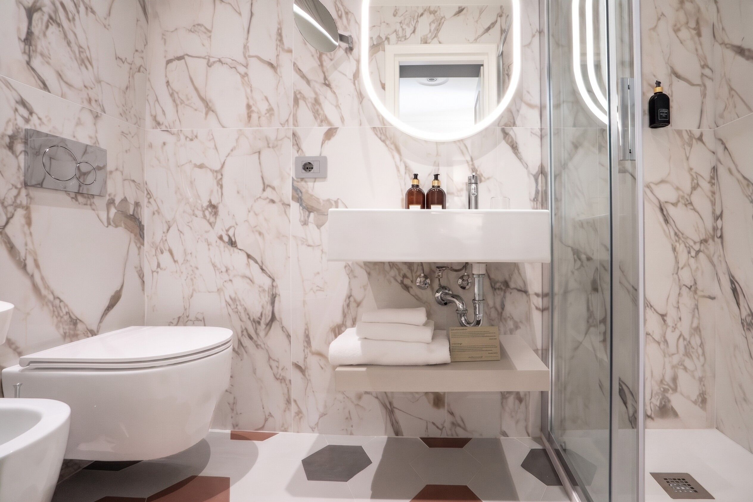A bathroom with a marble wall, a glass shower enclosure, a white sink, and a toilet.