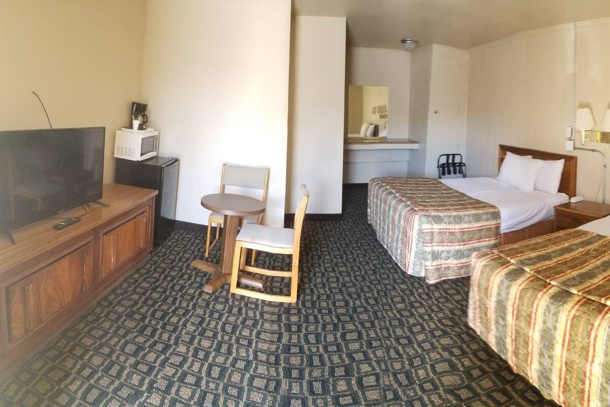 A hotel room with two beds, a desk with a TV, a chair, and a mirror.