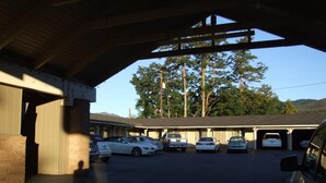 A parking area with several cars, a building with a flat roof, and trees in the background.