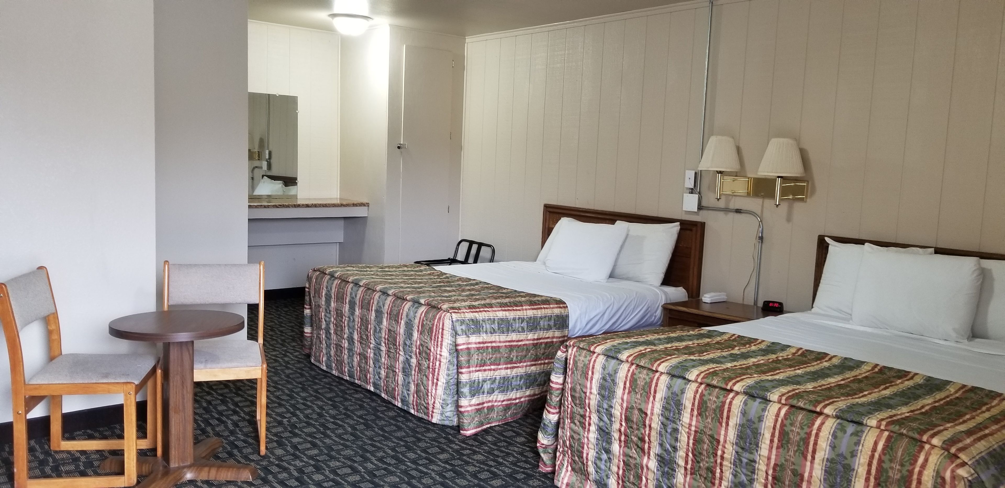 Une chambre d’hôtel avec deux lits, une petite table, une chaise, un bureau et un miroir.