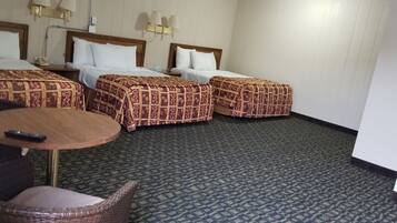 A hotel room with three beds, a round table, and a chair.