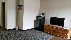 A hotel room with a patterned carpet, a television on a wooden cabinet, a microwave, and a small trash bin.