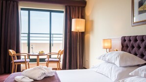 Une chambre d’hôtel avec un lit, deux chaises, une table, une lampe et une fenêtre avec des rideaux.