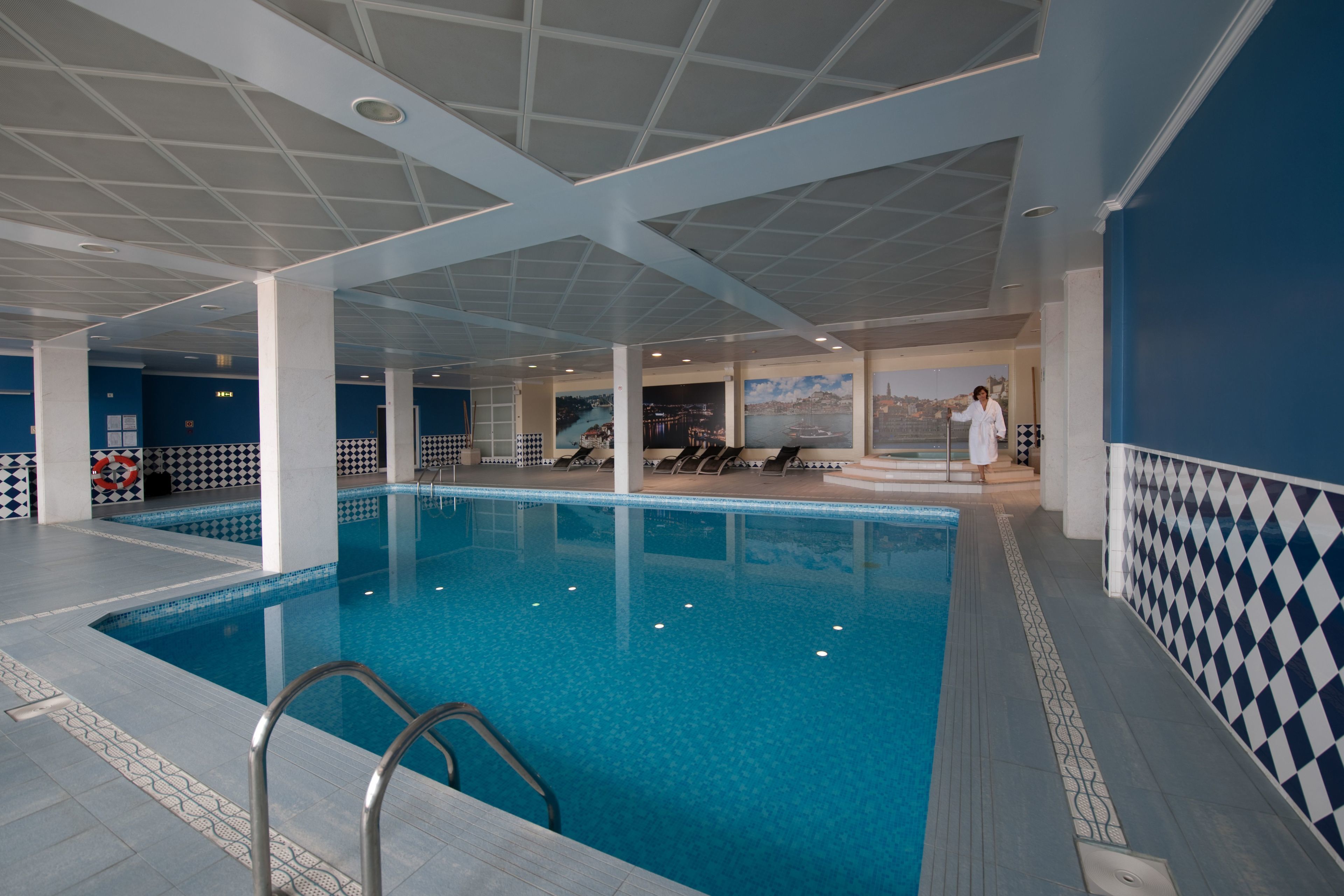 An indoor swimming pool with clear blue water, surrounded by white columns and blue walls.
